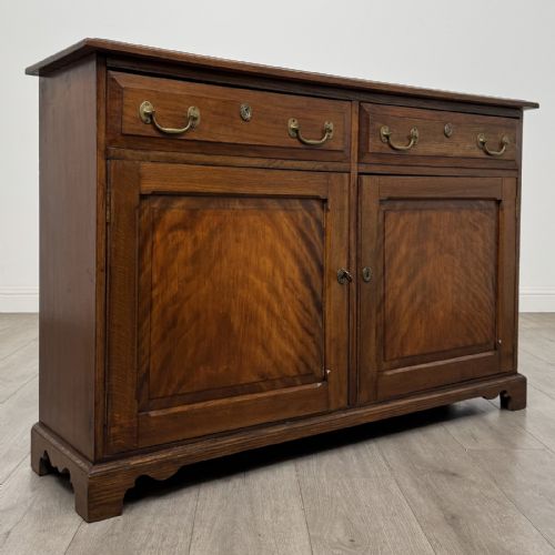 fig 7. A Georgian style warm brown oak dresser base featuring two drawers with brass drop handles above two panelled cupboard doors, raised on bracket feet.