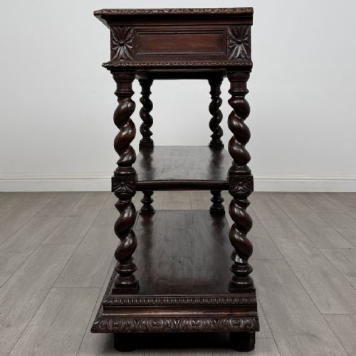 fig 2. A dark oak three-tier buffet featuring relief foliage carving across the top drawer frieze and four barley twist corner support legs.