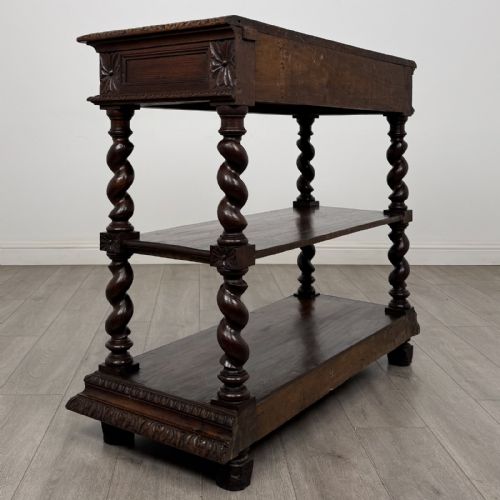 fig 3. A dark oak three-tier buffet featuring relief foliage carving across the top drawer frieze and four barley twist corner support legs.