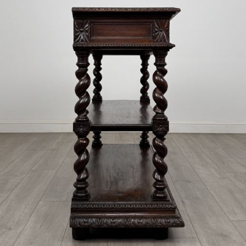 fig 6. A dark oak three-tier buffet featuring relief foliage carving across the top drawer frieze and four barley twist corner support legs.