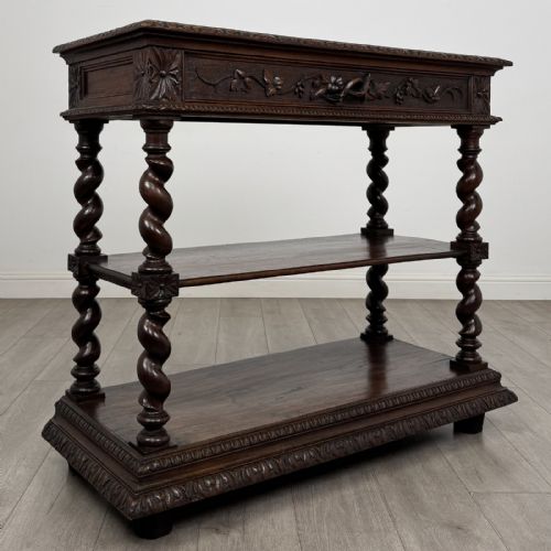 fig 7. A dark oak three-tier buffet featuring relief foliage carving across the top drawer frieze and four barley twist corner support legs.