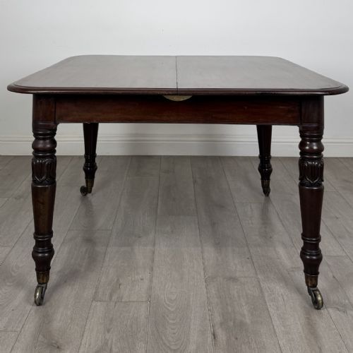 fig 1. An antique William IV mahogany extending dining table featuring a dark timber top with rounded corners, turned legs, and brass castors.