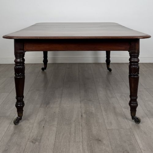 fig 2. An antique William IV mahogany extending dining table featuring a dark timber top with rounded corners, turned legs, and brass castors.