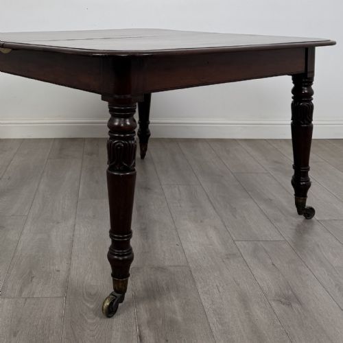 fig 3. An antique William IV mahogany extending dining table featuring a dark timber top with rounded corners, turned legs, and brass castors.