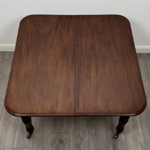 fig 4. An antique William IV mahogany extending dining table featuring a dark timber top with rounded corners, turned legs, and brass castors.