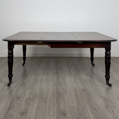 fig 5. An antique William IV mahogany extending dining table featuring a dark timber top with rounded corners, turned legs, and brass castors.