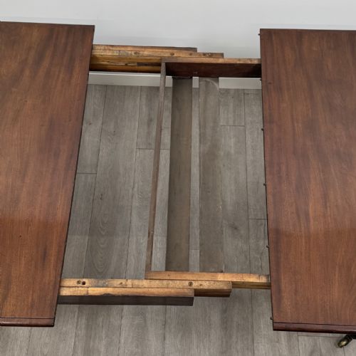 fig 6. An antique William IV mahogany extending dining table featuring a dark timber top with rounded corners, turned legs, and brass castors.