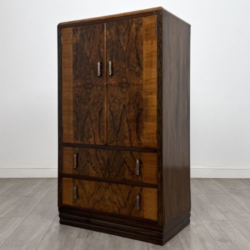 fig 1. An Art Deco walnut tallboy cabinet featuring highly figured book-matched veneer, double doors over two long drawers, vertical metal handles, and a stepped plinth base.