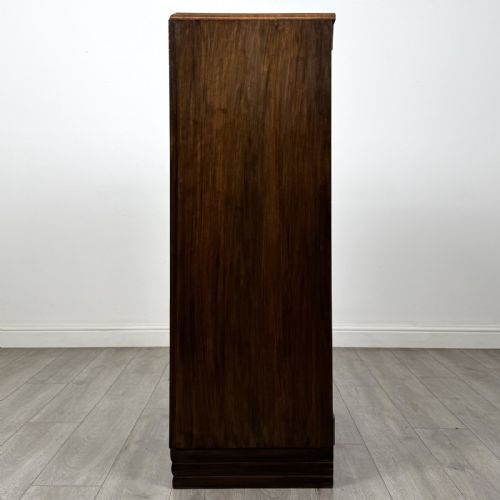 fig 2. An Art Deco walnut tallboy cabinet featuring highly figured book-matched veneer, double doors over two long drawers, vertical metal handles, and a stepped plinth base.