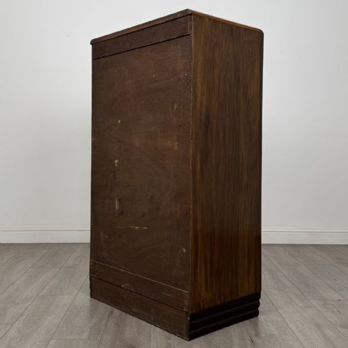 fig 5. An Art Deco walnut tallboy cabinet featuring highly figured book-matched veneer, double doors over two long drawers, vertical metal handles, and a stepped plinth base.