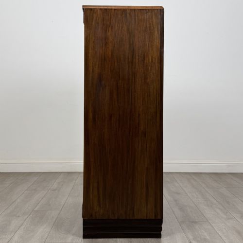 fig 6. An Art Deco walnut tallboy cabinet featuring highly figured book-matched veneer, double doors over two long drawers, vertical metal handles, and a stepped plinth base.