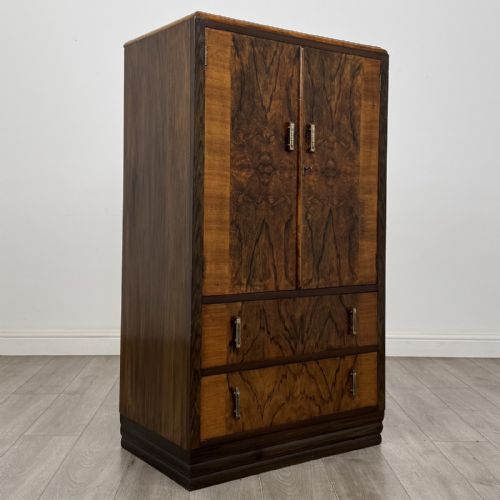 fig 7. An Art Deco walnut tallboy cabinet featuring highly figured book-matched veneer, double doors over two long drawers, vertical metal handles, and a stepped plinth base.