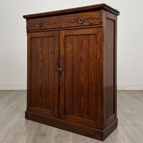 fig 1. A Victorian pitch pine cupboard featuring a single top drawer with brass drop ring handles above a two-door cabinet with vertical panelled detailing.