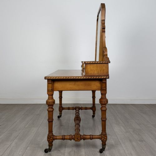 fig 2. An antique Victorian Gothic oak dressing table featuring a central adjustable swing mirror, pierced tracery supports, two upper trinket drawers, two main drawers, inlaid borders, turned legs, and brass ring handles.