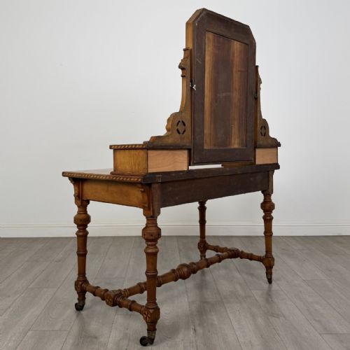 fig 3. An antique Victorian Gothic oak dressing table featuring a central adjustable swing mirror, pierced tracery supports, two upper trinket drawers, two main drawers, inlaid borders, turned legs, and brass ring handles.