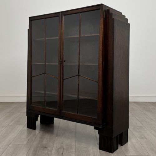 fig 1. A dark oak Art Deco display cabinet with two glazed doors, geometric glazing bars, stepped side shoulders, and reeded square feet.