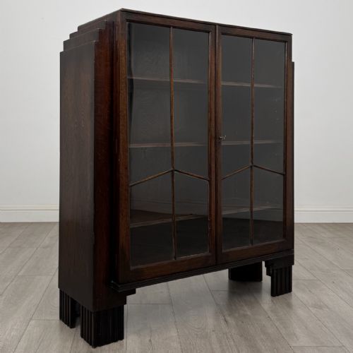 fig 7. A dark oak Art Deco display cabinet with two glazed doors, geometric glazing bars, stepped side shoulders, and reeded square feet.