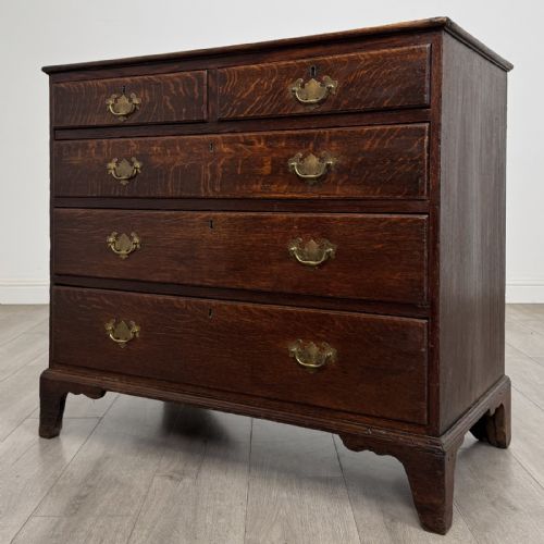 fig 1. An 18th-century dark oak Georgian chest of drawers featuring a two-short-over-three-long drawer configuration, brass handles, and bracket feet.