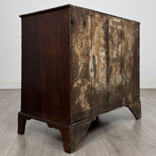 fig 3. An 18th-century dark oak Georgian chest of drawers featuring a two-short-over-three-long drawer configuration, brass handles, and bracket feet.