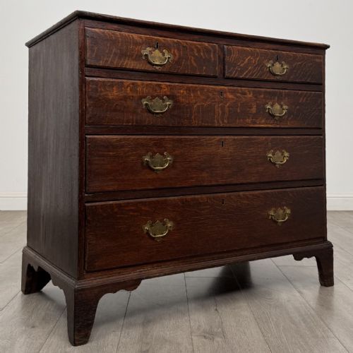 fig 7. An 18th-century dark oak Georgian chest of drawers featuring a two-short-over-three-long drawer configuration, brass handles, and bracket feet.
