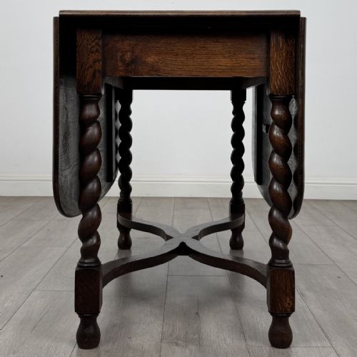 fig 2. A dark brown oak drop-leaf dining table with folded side leaves, barley twist legs, and a shaped cross-stretcher base.