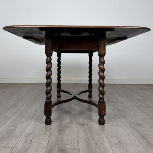 fig 3. A dark brown oak drop-leaf dining table with folded side leaves, barley twist legs, and a shaped cross-stretcher base.