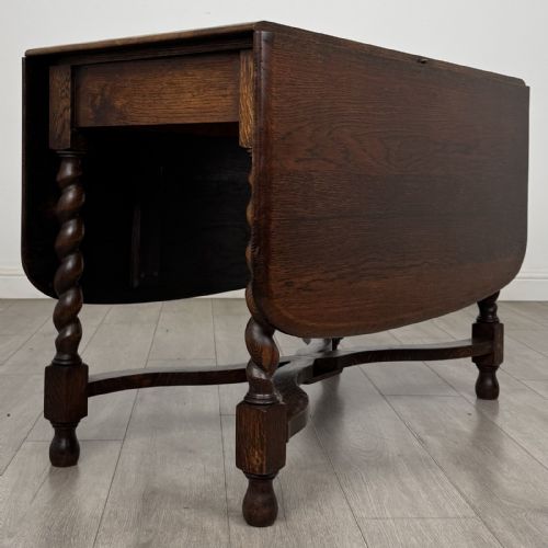 fig 4. A dark brown oak drop-leaf dining table with folded side leaves, barley twist legs, and a shaped cross-stretcher base.