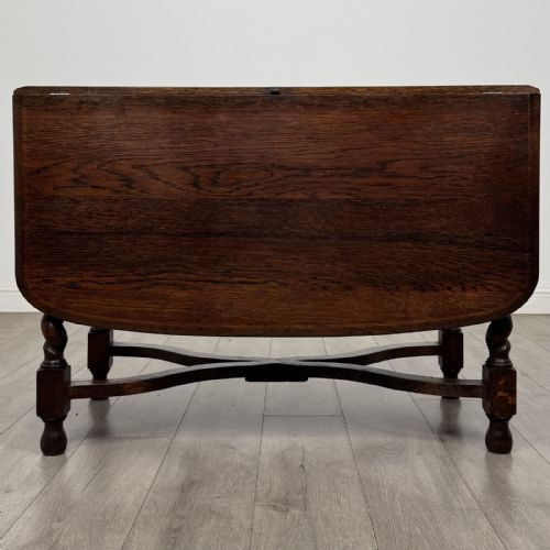 fig 5. A dark brown oak drop-leaf dining table with folded side leaves, barley twist legs, and a shaped cross-stretcher base.