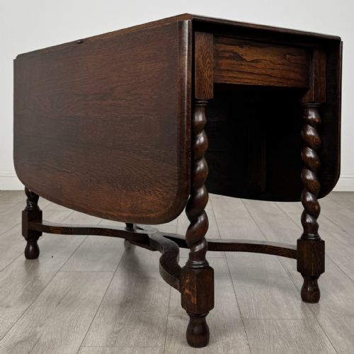 fig 6. A dark brown oak drop-leaf dining table with folded side leaves, barley twist legs, and a shaped cross-stretcher base.