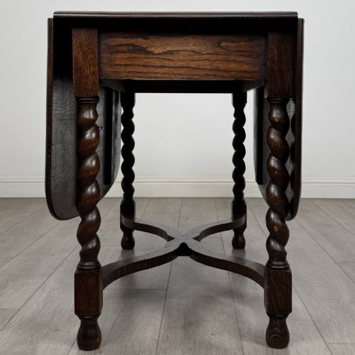fig 7. A dark brown oak drop-leaf dining table with folded side leaves, barley twist legs, and a shaped cross-stretcher base.