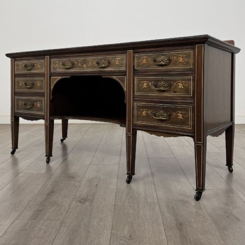 fig 1. An Edwardian mahogany sideboard featuring detailed foliate marquetry inlay, seven drawers with brass handles, an arched central apron, and tapered legs with castors.