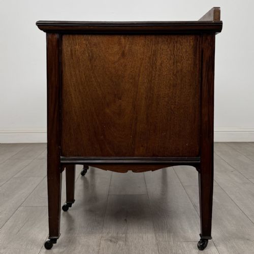 fig 2. An Edwardian mahogany sideboard featuring detailed foliate marquetry inlay, seven drawers with brass handles, an arched central apron, and tapered legs with castors.