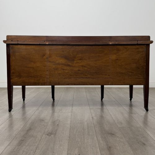 fig 4. An Edwardian mahogany sideboard featuring detailed foliate marquetry inlay, seven drawers with brass handles, an arched central apron, and tapered legs with castors.
