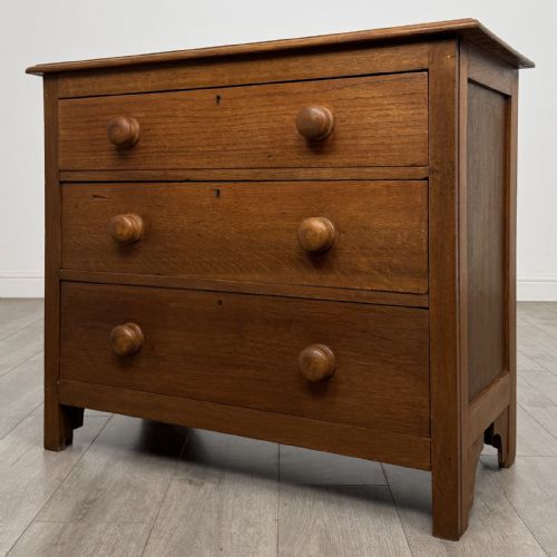 fig 1. A small 20th-century warm brown oak chest of drawers featuring three wide drawers with turned wooden knobs.