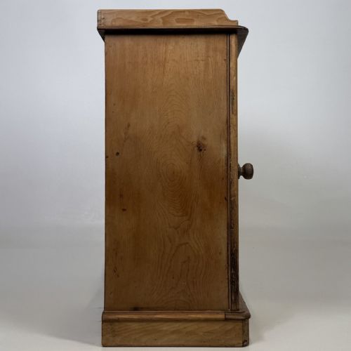 fig 6. An antique natural pine pot cupboard featuring a single arched panel door, turned wooden knob handle, side top galleries, and a solid plinth base.