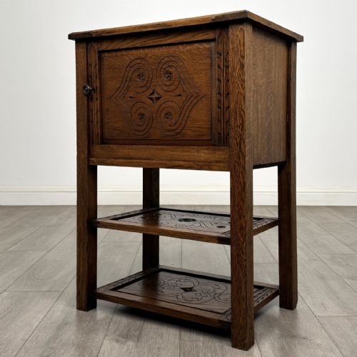 fig 1. A dark carved oak cabinet featuring a single door adorned with scrolling strapwork designs situated above two open lower shelves.