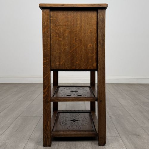 fig 2. A dark carved oak cabinet featuring a single door adorned with scrolling strapwork designs situated above two open lower shelves.