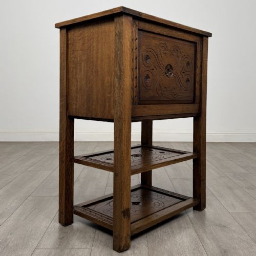 fig 3. A dark carved oak cabinet featuring a single door adorned with scrolling strapwork designs situated above two open lower shelves.