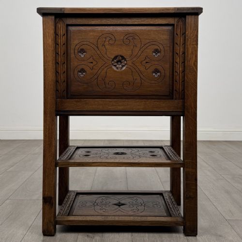 fig 4. A dark carved oak cabinet featuring a single door adorned with scrolling strapwork designs situated above two open lower shelves.