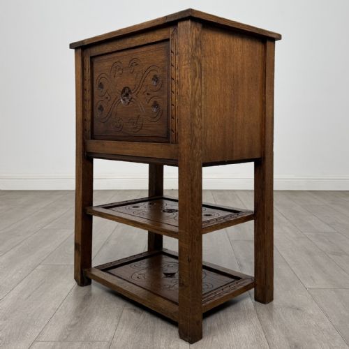 fig 5. A dark carved oak cabinet featuring a single door adorned with scrolling strapwork designs situated above two open lower shelves.