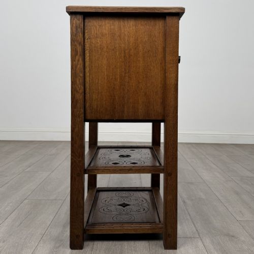 fig 6. A dark carved oak cabinet featuring a single door adorned with scrolling strapwork designs situated above two open lower shelves.