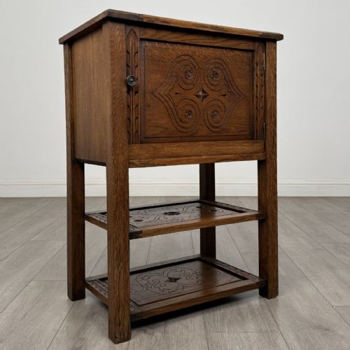 fig 7. A dark carved oak cabinet featuring a single door adorned with scrolling strapwork designs situated above two open lower shelves.
