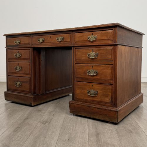 fig 1. A 19th-century walnut pedestal desk featuring nine drawers with brass handles and a plinth base.