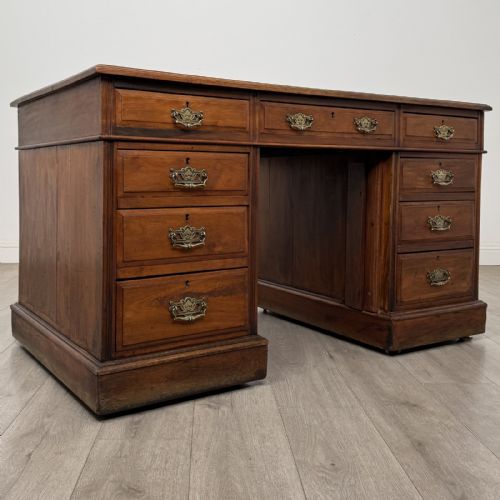 fig 7. A 19th-century walnut pedestal desk featuring nine drawers with brass handles and a plinth base.