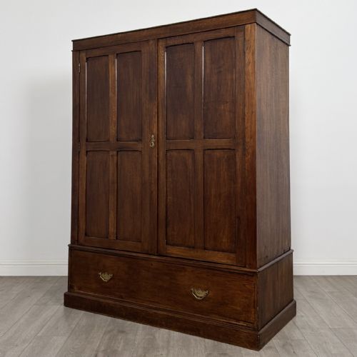 fig 1. A tall dark oak Edwardian wardrobe featuring double panelled doors above a single full-width base drawer with brass drop handles.