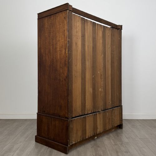 fig 3. A tall dark oak Edwardian wardrobe featuring double panelled doors above a single full-width base drawer with brass drop handles.