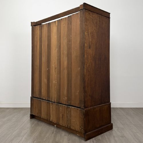 fig 5. A tall dark oak Edwardian wardrobe featuring double panelled doors above a single full-width base drawer with brass drop handles.
