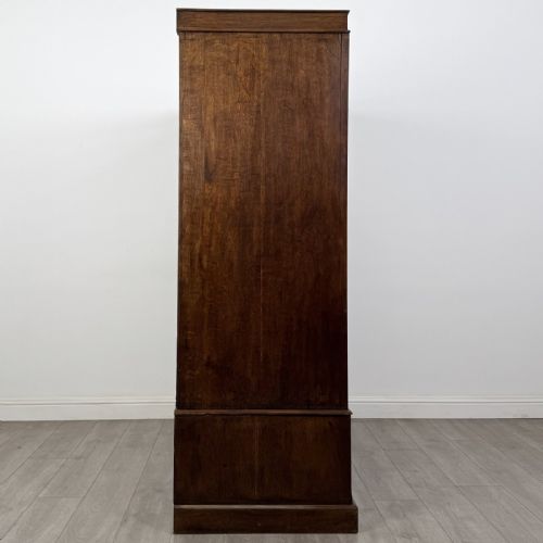 fig 6. A tall dark oak Edwardian wardrobe featuring double panelled doors above a single full-width base drawer with brass drop handles.