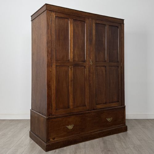 fig 7. A tall dark oak Edwardian wardrobe featuring double panelled doors above a single full-width base drawer with brass drop handles.