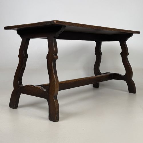 fig 3. A dark brown oak low coffee table featuring a rectangular plank top supported by shaped trestle end legs joined by a low central stretcher.